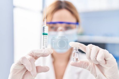 Photo for Young blonde woman scientist wearing medical mask holding covid-19 vaccine at laboratory - Royalty Free Image