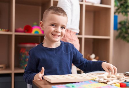 Téléchargez les photos : Adorable garçon caucasien jouer avec jeu de puzzle assis sur la table à la maternelle - en image libre de droit