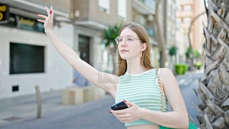Foto de Mujer rubia joven usando smartphone pidiendo taxi en la calle - Imagen libre de derechos