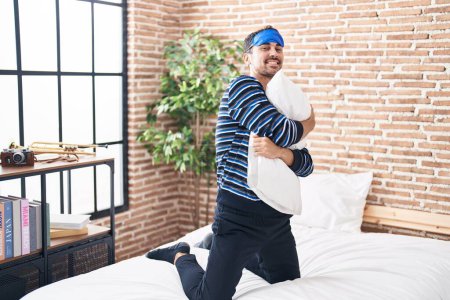 Téléchargez les photos : Young hispanic man wearing sleep mask hugging pillow at bedroom - en image libre de droit