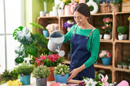 Téléchargez les photos : Young beautiful hispanic woman florist smiling confident watering plant at flower shop - en image libre de droit