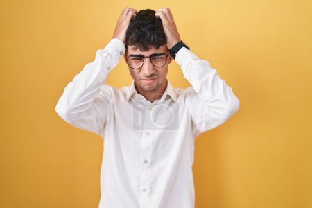 Photo for Young hispanic man standing over yellow background suffering from headache desperate and stressed because pain and migraine. hands on head. - Royalty Free Image