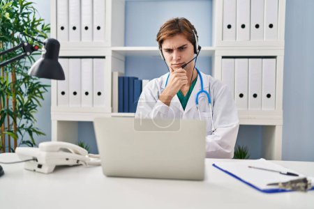 Photo for Young doctor man working on online appointment serious face thinking about question with hand on chin, thoughtful about confusing idea - Royalty Free Image