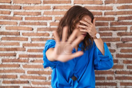 Photo for Beautiful brunette woman standing over bricks wall covering eyes with hands and doing stop gesture with sad and fear expression. embarrassed and negative concept. - Royalty Free Image