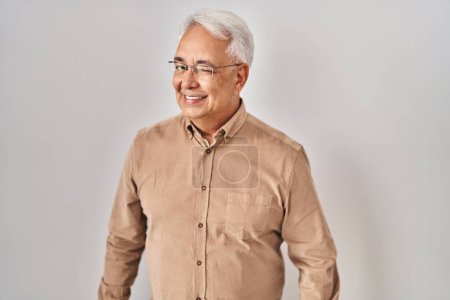 Téléchargez les photos : Hispanique senior homme portant des lunettes clin d'oeil en regardant la caméra avec une expression sexy, gai et heureux visage. - en image libre de droit