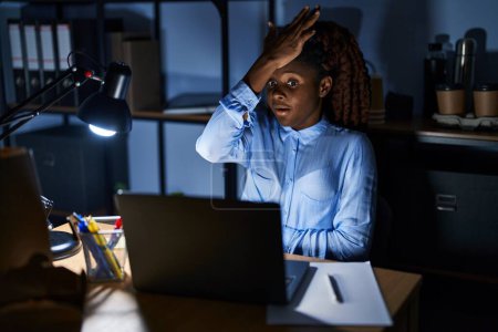 Téléchargez les photos : Femme africaine travaillant au bureau la nuit surpris avec la main sur la tête pour erreur, rappelez-vous erreur. oublié, mauvais concept de mémoire. - en image libre de droit