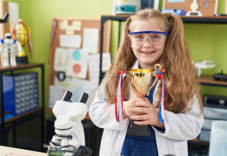 Photo for Adorable blonde girl student smiling confident holding gold trophy at laboratory classroom - Royalty Free Image