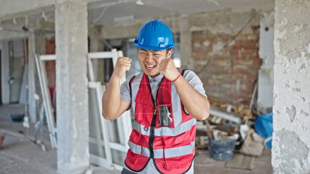 Téléchargez les photos : Constructeur souriant avec l'expression gagnante sur le chantier de construction - en image libre de droit