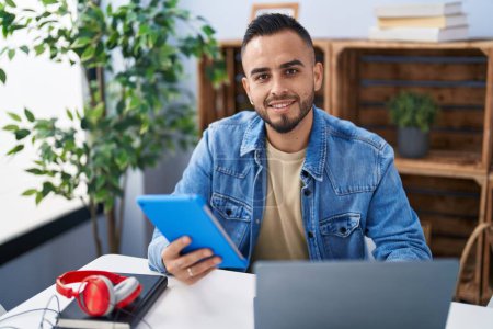 Téléchargez les photos : Jeune homme hispanique utilisant touchpad et ordinateur portable assis sur la table à la maison - en image libre de droit