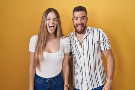 Téléchargez les photos : Jeune couple debout sur fond jaune langue collante heureux avec une expression drôle. concept d'émotion. - en image libre de droit