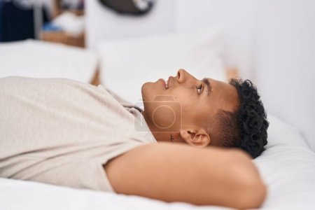 Téléchargez les photos : Jeune homme latino souriant confiant couché sur le lit dans la chambre - en image libre de droit