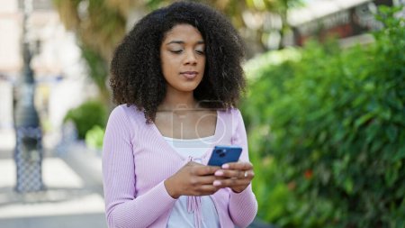 Foto de Mujer afroamericana usando smartphone con expresión seria en el parque - Imagen libre de derechos