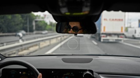 Téléchargez les photos : Moyen Age femme hispanique conduisant une voiture portant des lunettes de soleil sur la route - en image libre de droit