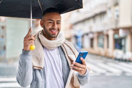 Téléchargez les photos : African american man using smartphone holding umbrella at street - en image libre de droit