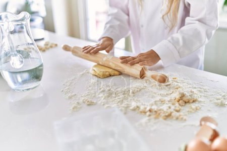 Foto de Young woman wearing cook uniform kneading pasta dough at kitchen - Imagen libre de derechos