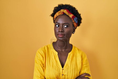 Foto de Mujer joven africana vistiendo turbante africano sonriendo mirando hacia un lado y mirando hacia otro pensando. - Imagen libre de derechos
