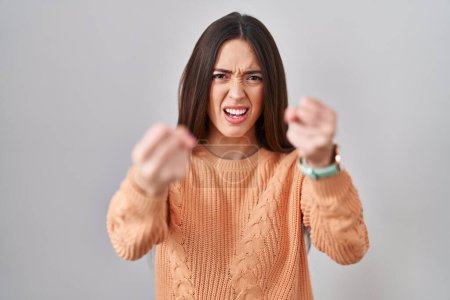 Photo for Young brunette woman standing over white background angry and mad raising fists frustrated and furious while shouting with anger. rage and aggressive concept. - Royalty Free Image