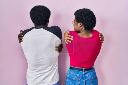 Foto de Joven pareja afroamericana de pie sobre fondo rosa abrazándose feliz y positivo desde atrás. amor propio y cuidado personal - Imagen libre de derechos