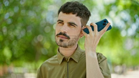 Photo for Young hispanic man listening to voice message at park - Royalty Free Image