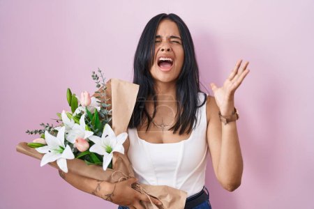 Photo for Brunette woman holding bouquet of white flowers crazy and mad shouting and yelling with aggressive expression and arms raised. frustration concept. - Royalty Free Image