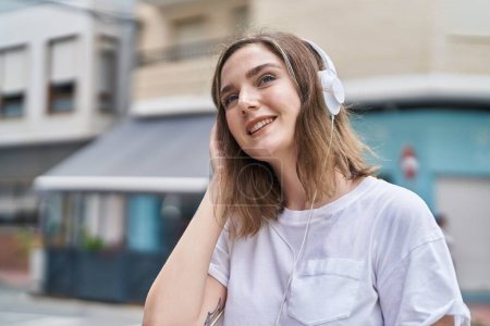 Téléchargez les photos : Jeune femme souriante à l'écoute de la musique dans la rue - en image libre de droit