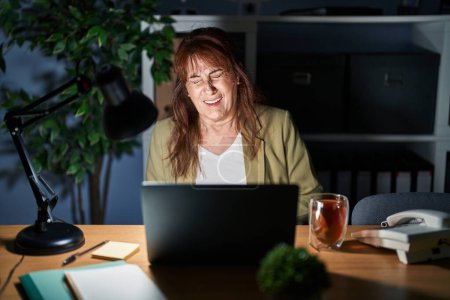 Photo for Middle age hispanic woman working using computer laptop at night with hand on stomach because nausea, painful disease feeling unwell. ache concept. - Royalty Free Image