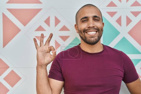 Photo for Hispanic man with beard standing over colorful wall doing ok sign with fingers, smiling friendly gesturing excellent symbol - Royalty Free Image