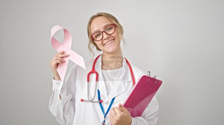 Foto de Joven mujer rubia médico sosteniendo el cáncer de mama conciencia cinta rosa y portapapeles sobre fondo blanco aislado - Imagen libre de derechos