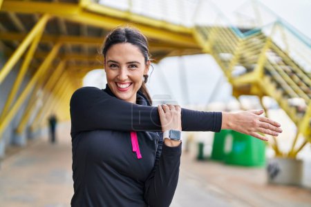 Photo for Young hispanic woman wearing sportswear stretching arms at street - Royalty Free Image