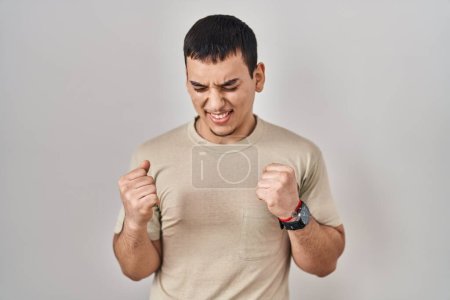 Téléchargez les photos : Jeune homme arabe portant t-shirt décontracté très heureux et excité faire geste gagnant avec les bras levés, souriant et criant pour le succès. concept de célébration. - en image libre de droit