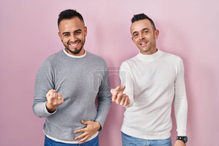 Téléchargez les photos : Couple homosexuel debout sur fond rose appel viennent ici geste avec la main invitant accueillant heureux et souriant - en image libre de droit