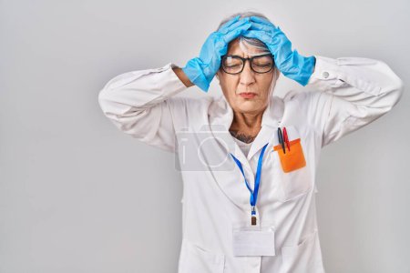 Photo for Middle age woman with grey hair wearing scientist robe suffering from headache desperate and stressed because pain and migraine. hands on head. - Royalty Free Image