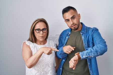 Téléchargez les photos : Mère hispanique et son fils debout ensemble dans la hâte pointant pour regarder le temps, l'impatience, bouleversé et en colère pour retard de la date limite - en image libre de droit