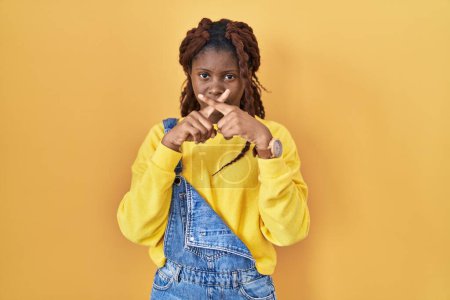 Photo for African woman standing over yellow background rejection expression crossing fingers doing negative sign - Royalty Free Image