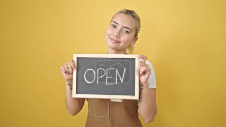 Photo for Young beautiful hispanic woman wearing apron holding open blackboard over isolated yellow background - Royalty Free Image