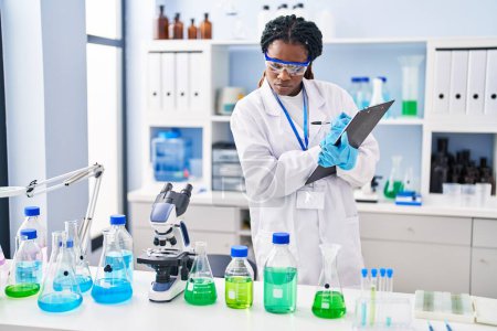 Téléchargez les photos : Femme scientifique afro-américaine rédigeant un rapport travaillant au laboratoire - en image libre de droit