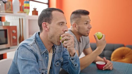 Photo for Two men couple sitting on table eating apple at dinning room - Royalty Free Image