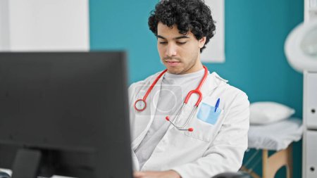 Photo for Young latin man doctor using computer working at clinic - Royalty Free Image