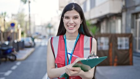 Foto de Joven hermosa mujer hispana teniendo encuesta entrevista escribiendo en portapapeles en la calle - Imagen libre de derechos