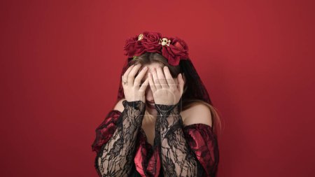 Foto de Mujer rubia joven con traje de katrina cubriendo la cara con las manos sobre el fondo rojo aislado - Imagen libre de derechos
