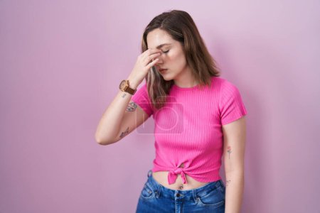 Foto de Blonde caucasian woman standing over pink background tired rubbing nose and eyes feeling fatigue and headache. stress and frustration concept. - Imagen libre de derechos