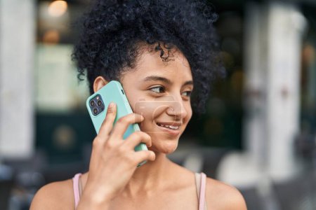 Téléchargez les photos : Jeune femme hispanique souriant confiant parler sur le smartphone à la rue - en image libre de droit