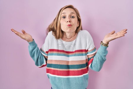 Photo for Young blonde woman standing over pink background clueless and confused expression with arms and hands raised. doubt concept. - Royalty Free Image