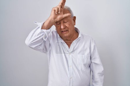 Téléchargez les photos : Senior man with grey hair standing over isolated background making fun of people with fingers on forehead doing loser gesture mocking and insulting. - en image libre de droit