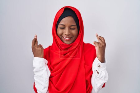 Téléchargez les photos : Jeune femme arabe portant l'écharpe traditionnelle islamique hijab geste doigt croisé souriant avec espoir et les yeux fermés. chance et concept superstitieux. - en image libre de droit