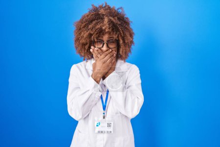 Photo for Young hispanic woman with curly hair wearing white coat and id card shocked covering mouth with hands for mistake. secret concept. - Royalty Free Image