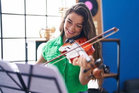 Foto de Joven mujer hispana músico sonriendo confiado tocando violín en el estudio de música - Imagen libre de derechos