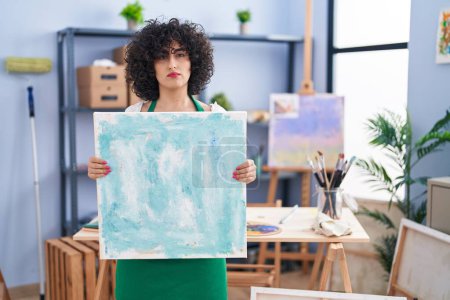 Photo for Young brunette woman with curly hair holding painter canvas relaxed with serious expression on face. simple and natural looking at the camera. - Royalty Free Image