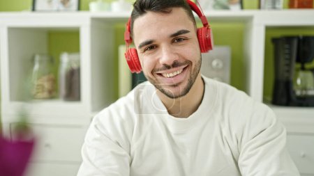 Photo for Young hispanic man listening to music sitting on table at dinning room - Royalty Free Image