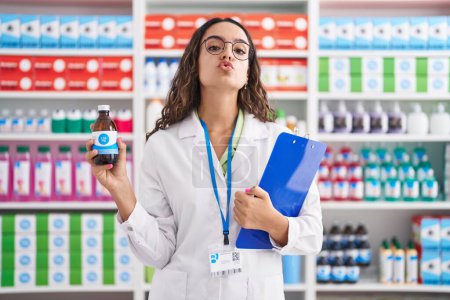 Photo for Young hispanic woman working at pharmacy drugstore holding syrup looking at the camera blowing a kiss being lovely and sexy. love expression. - Royalty Free Image